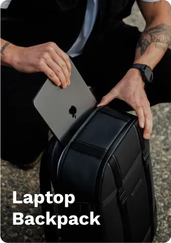 Black laptop backpack with a padded compartment, shown being packed with a silver laptop, on a gravel surface.