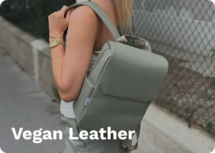 Green vegan leather backpack with adjustable straps, worn by a person, standing on a sidewalk near a chain-link fence.