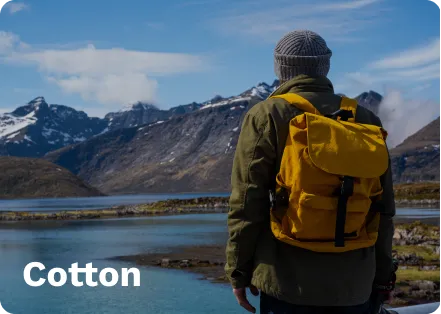 Yellow cotton backpack with black straps, worn by a person in a gray hat and green jacket, overlooking a lake and snowy mountains.