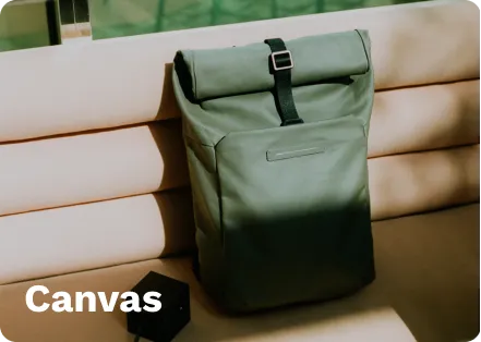 Olive green roll-top backpack with black straps and buckle, placed on a beige couch, with a small black device nearby.