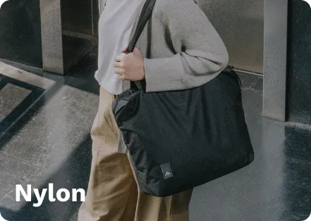 Black nylon tote bag with a branded logo, carried by a person, walking on a shiny floor near a metal structure. Reply