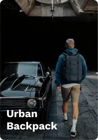 Dark gray urban backpack with adjustable straps, worn by a person walking near a black classic car under a concrete overpass.