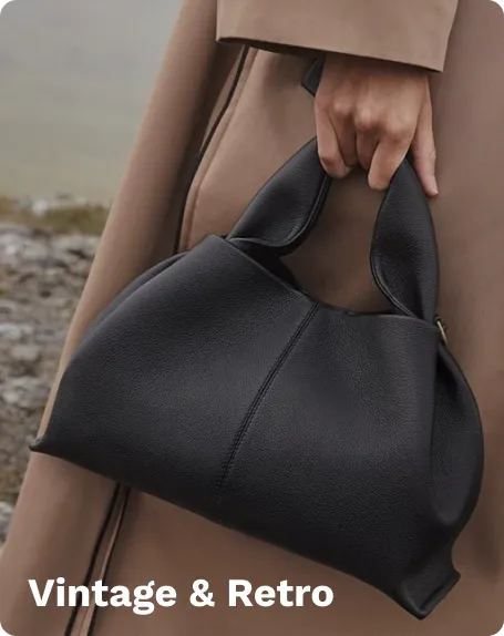 Black vintage and retro leather bag with unique ear-shaped handles, held by a person, standing outdoors near rocky terrain.