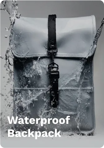 Gray waterproof backpack with black straps and buckles, shown being splashed with water, demonstrating durability on a gray background.