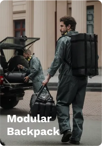 Black modular backpack with adjustable straps, worn by a person walking on a street, near a vehicle with another black modular bag being loaded.