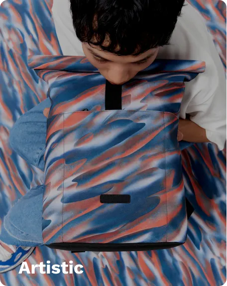 Colorful artistic backpack with red, blue, and orange swirl patterns, worn by a person, set against a matching abstract background.